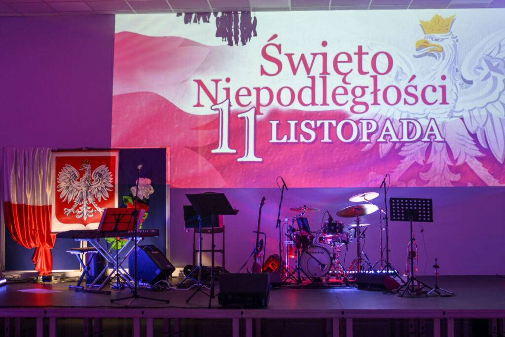 Scena z instrumentami, tło z napisem Święto Niepodległości 11 listopada, dominują kolory biały i czerwony.