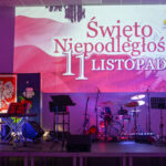 Scena z instrumentami, tło z napisem Święto Niepodległości 11 listopada, dominują kolory biały i czerwony.