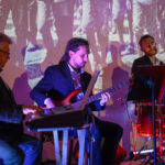 Trzech muzyków gra: jeden na klawiszach, drugi na gitarze basowej, trzeci na perkusji. Tło z projekcją w sepii. Oświetlenie purpurowe i czerwone.