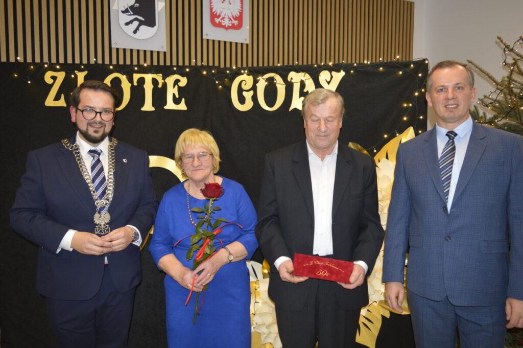 Cztery osoby pozują przed czarnym tłem z napisem Złote Gody. Kobieta w niebieskiej sukni trzyma czerwoną różę. Mężczyźni mają na sobie ciemne garnitury.