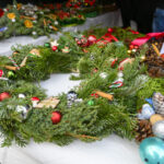 Świąteczne wieńce z zielonej jodły, ozdobione czerwonymi i srebrnymi bombkami oraz szyszkami, leżą na białym obrusie.