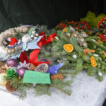 Świąteczne wieńce na białym obrusie, ozdobione czerwoną wstążką, suszonymi pomarańczami i szyszkami. Tło ciemne.