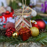 Świąteczna kompozycja z bombkami i gałązkami. Szklany słoik ozdobiony czerwono-białym domkiem. Tło rozmyte, kolorowe detale.