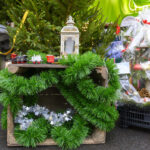 Zielona girlanda ozdabia drewnianą skrzynkę z małym pociągiem i latarnią. W tle choinki i świąteczne dekoracje. Jasne, świąteczne kolory.