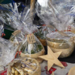 Drewniane miski w przezroczystej folii, obok drewniana gwiazdka. Tło jest ciemne, z kolorowymi tkaninami i rękodziełem.