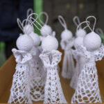 Ręcznie robione anioły z białego materiału w pudełku. Jasne tło z zielonym akcentem. Anioły mają koronkowe detale.