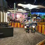 611011229_2897767463749666_4992009826121482617_n Jasno oświetlona karuzela w wesołym miasteczku, widoczne dzieci na siedzeniach. Barwne tło z motywem zimowym. Kolorowe, drewniane ogrodzenie.