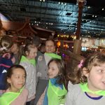 619597260_4209730689294176_4968684710147169194_n Grupa dzieci w jaskrawych, zielonych kamizelkach stoi w pomieszczeniu przypominającym park rozrywki. Widać drewniane konstrukcje i światełka w tle. Dzieci są uśmiechnięte i rozmawiają ze sobą.