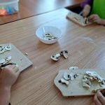 Dzieci kroją pieczarki na deskach do krojenia na drewnianym stole. Na stole znajdują się również miska i pokrojone pieczarki. Tło jest spokojne, kolory naturalne.