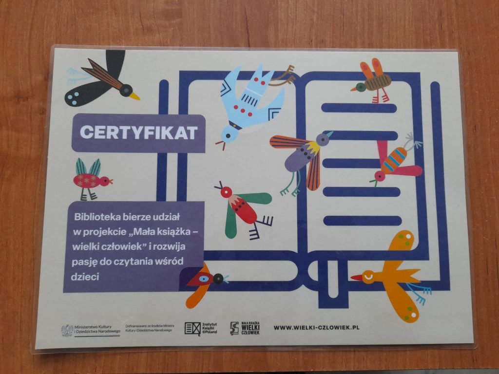 Certyfikat z kolorowymi ptakami na beżowym tle. Podkreśla udział biblioteki w projekcie czytelniczym dla dzieci. Tekst w fioletowych prostokątach.