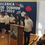 637011345_931741195868069_3125439886104697789_n Grupa uczniów w białych koszulach stoi na scenie, czytając przy mikrofonach. Za nimi niebieska plansza z napisem Rocznica bitwy pod Dobrem 1831-2026, ozdobiona czerwonymi i białymi różami. Po prawej stronie