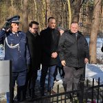 639568767_931740199201502_5404822595109635012_n Grupa mężczyzn w zimowych ubraniach stoi przy ogrodzeniu w lesie. Policjant w mundurze salutuje. Tło jest zaśnieżone i słoneczne.