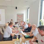 651925488_951497053892483_2886693486125518186_n Grupa osób siedzi przy stole w jasnym pomieszczeniu, wszyscy ubrani w białe koszulki. Na ścianie widać baner z napisem Mazowsze. Na stole znajdują się napoje i dokumenty.