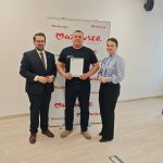 652329535_951497843892404_8544871621828777854_n Trzy osoby stoją na tle baneru z napisem Mazowsze. Jedna osoba trzyma certyfikat. Sala ma jasne ściany i drewnianą podłogę.