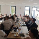 652467049_951496343892554_8290417103224747510_n Spotkanie osób siedzących przy długim stole w jasnej sali. Na ścianie widoczne logotypy Mazowsze i Gmina Dobre. Przez okna wpada światło słoneczne.