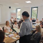 653068235_951495733892615_7015472885809857936_n Spotkanie ludzi przy stole w jasnym pomieszczeniu z oknami. Na ścianie logo Mazowsze, panuje profesjonalna atmosfera. W tle krzyż na ścianie.