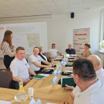 653457788_951498913892297_6090219787976372356_n Na zdjęciu grupa ludzi w białych koszulkach siedzi przy stole. W tle prezentacja z napisem Konwent Sołtysów. Sala jest jasna, z polską flagą w rogu.