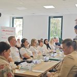 653635810_951497117225810_5669253179663092848_n Spotkanie grupy ludzi przy stole konferencyjnym w jasnym pokoju z krzyżem. W tle transparent Mazowsze. Serce Polski. Uczestnicy w białych koszulkach, jedna osoba mówi.