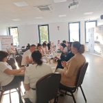 653700848_951495613892627_3626464169678289453_n Spotkanie przy długim stole w jasnej sali z oknami. Osoby siedzące w krzesłach rozmawiają. Na ścianach widoczne plakaty.