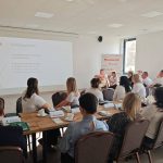653700910_951495793892609_8933771380188822679_n Grupa ludzi siedzi przy stole w sali konferencyjnej, oglądając prezentację na temat funduszu sołeckiego. Jasne wnętrze, duży ekran z wykresem, białe ściany. Za nimi widoczne okno i baner z napisem Mazowsze.