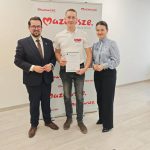 653705337_951498107225711_7856723911986272507_n Trzy osoby stoją przed banerem z napisem Mazowsze. Lewa osoba w garniturze, środkowa trzyma dyplom, prawa w niebieskiej koszuli. Tło jest jasne, podłoga drewniana.