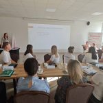 654340802_951496627225859_6885228188009965623_n Spotkanie w sali konferencyjnej z prezentacją na białym ekranie. Ludzie siedzą przy stołach, przeważają jasne kolory wnętrza. Tło ozdabia logo Mazowsze.