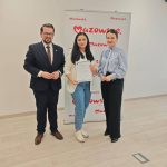 654583657_951498463892342_2947783802119325225_n Trzy osoby stoją przed rozwiniętym banerem z napisem Mazowsze. Kobieta w środku trzyma certyfikat. Tło jest jasne.