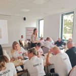 654985070_951496840559171_1578782715391292317_n Na zdjęciu jest grupa ludzi w białych koszulkach przy stole. Tło to jasne, przestronne pomieszczenie z dużymi oknami. Na ekranie widoczny jest napis Mazowsze.