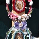 Dwa ozdobne wianki z kwiatami i zdjęciami królików na beżowym tle. Jeden w kolorze czerwonym, drugi niebieski. Ozdobione białymi kwiatkami i jajkami.