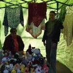 Dwie osoby w namiocie z zielonym wnętrzem. Na stole kolorowe, szydełkowe zabawki. W tle zawieszone różnobarwne chusty.