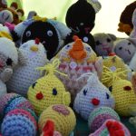 Kolorowe, ręcznie robione szydełkowe zabawki w kształcie zwierząt. Różnorodne odcienie włóczki, tło neutralne. Każda zabawka ma cenę.