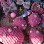 Koszyk z różnymi ozdobami. Różowe, ozdobione perłami jajka z przędzy. W tle kolorowe wstążki i mała gumowa kaczuszka.