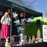 Scena z zielonym namiotem, z przodu dekoracje z królikami wielkanocnymi. Kobieta w różowej spódnicy przemawia do mikrofonu. W tle logo Mazowsze.