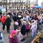 Na zdjęciu widać tłum ludzi na jarmarku na świeżym powietrzu. Stoiska z kolorowymi namiotami są tłem. Wszyscy ubrani są ciepło, choć pogoda jest jasna.