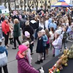 Zdjęcie przedstawia tłum ludzi na zewnątrz, głównie dzieci w kolorowych kurtkach. W tle namioty z zielonymi i biało-niebieskimi daszkami. Na pierwszym planie dekoracje w kształcie zajączków.