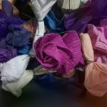 Kolorowe papierowe róże, głównie w odcieniach różu, fioletu i bieli, z zielonymi drucikami, na ciemnym tle.