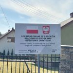 667742050_967881195587402_2161279605619724258_n Tablica informacyjna z białym tłem i napisem o dofinansowaniu z programu odbudowy zabytków. Widoczne flagi Polski oraz godło. W tle domy, zielone podwórko i niebo.