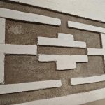 6FGVIZsD Tekstura ściany z wzorem geometrycznym, białe elementy na szarym tle. Układ prostokątów i krzyży stanowi dekorację.