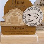 Trofeum z drewna przedstawia Muzeum Konstantego Laszczki i portret mężczyzny. Tło jest jasnobrązowe. Napis: I miejsce za bieg na 6 km.