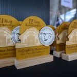 Złote statuetki z napisem II Bieg Konstantego na drewnianej podstawie. Obok medal z wizerunkiem mężczyzny. Tło jest niebieskie.
