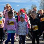 Dzieci w kolorowych ubraniach z numerami startowymi na ulicy. W tle niebo i drzewa. Atmosfera pełna energii i oczekiwania.