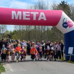 Zdjęcie przedstawia start biegu dzieci pod różowo-niebieskim łukiem z napisem META. W tle widoczni są kibice oraz drzewa. Na niebie znajdują się białe chmury.