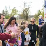 Grupa ludzi na zewnątrz odbiera medale. W tle drzewa i niebo. Ubrani w kolorowe stroje sportowe.