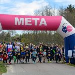 Start dziecięcego biegu pod różowo-niebieskim łukiem z napisem META. Tło to drzewa i niebo. Liczny tłum kibiców.