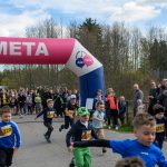Dzieci biegną przez różowy łuk z napisem META. W tle jest tłum ludzi i drzewa. Pogoda jest słoneczna, a niebo jasnoniebieskie.
