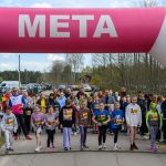 Zdjęcie przedstawia start biegu dzieci pod różowym łukiem z napisem META. W tle zieleń i zaparkowane samochody. Grupa młodych uczestników stoi na starcie, gotowa do biegu.