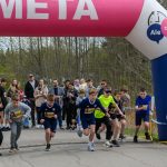 Grupa dzieci startuje w biegu spod różowego łuku z napisem META. W tle są drzewa i tłum ludzi. Dzień jest pochmurny.