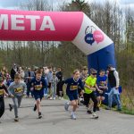 Na zdjęciu grupa dzieci startuje w biegu pod różowym łukiem z napisem META. Tło stanowią drzewa i kibicujący ludzie. Dzieci mają na sobie kolorowe stroje sportowe.