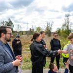 Grupa ludzi na zewnątrz, chłopiec w koszulce z numerem 265 otrzymuje gratulacje. W tle drzewa i pochmurne niebo.