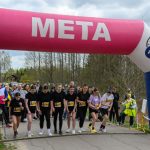 Start biegu pod różowo-białym łukiem z napisem META. Grupa zawodników stoi na starcie. W tle drzewa i widzowie.
